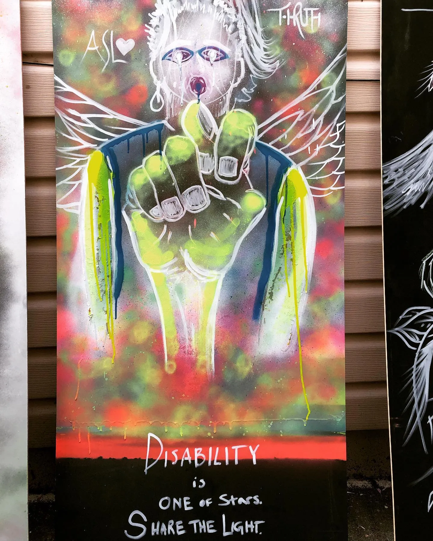 An ASL Love spray-painted art panel previewed for Burning Man 2019. A glowing neon-green ASL fist handshape rises from a winged, weeping figure against a fiery red-and-green cosmic background. Hand-lettered text reads 'ASL' with a heart, 'T-TRUTH,' and along the bottom: 'DISABILITY is one of stars. Share the Light.'